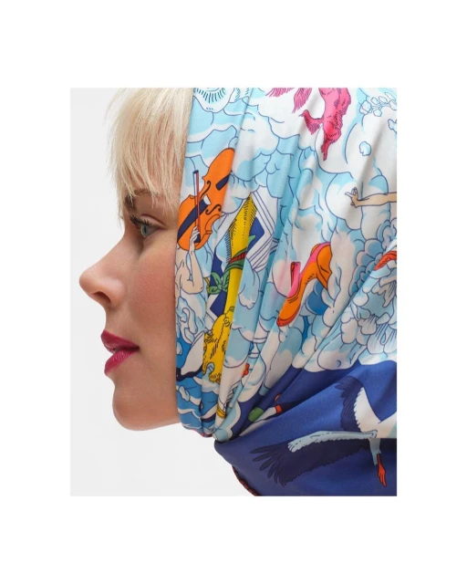 Woman wearing a colorful patterned headscarf with musical and crane illustrations against a bright white background in a profile shot.