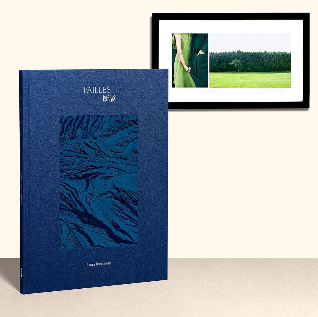 A blue photography book titled 'Failles' stands next to a framed image of a green landscape with a person, against a light background.