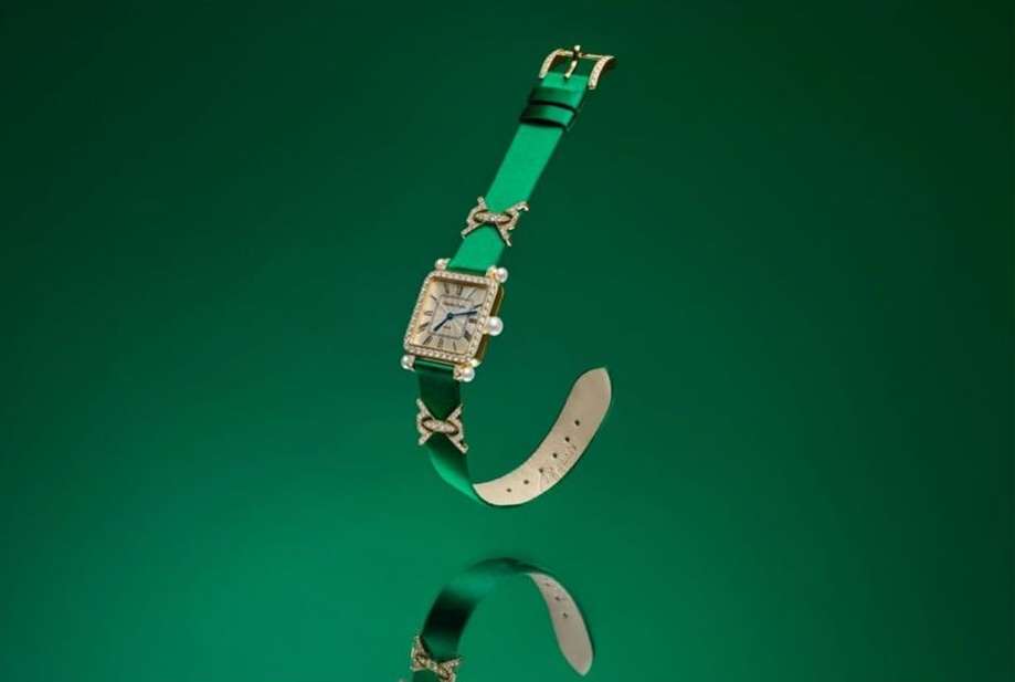 Elegant square-faced watch with gold detailing and a green strap, displayed on a reflective green surface creating a mirrored effect.