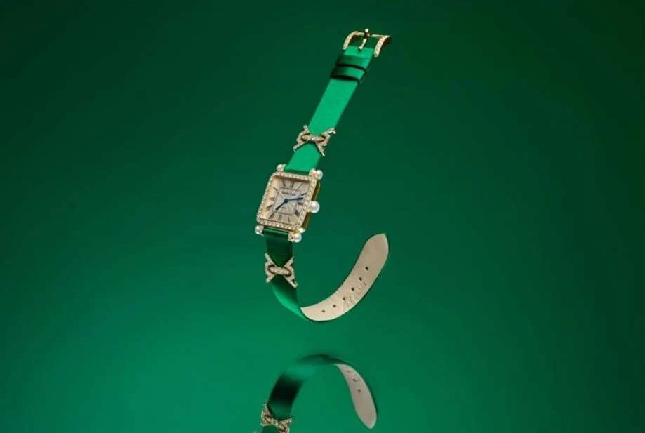 Elegant square-faced watch with gold detailing and a green strap, displayed on a reflective green surface creating a mirrored effect.