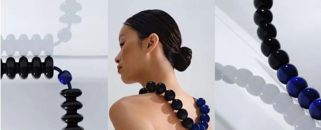 Woman with black and blue bead necklace posing in front of light grey studio background with modern white and black beaded design.