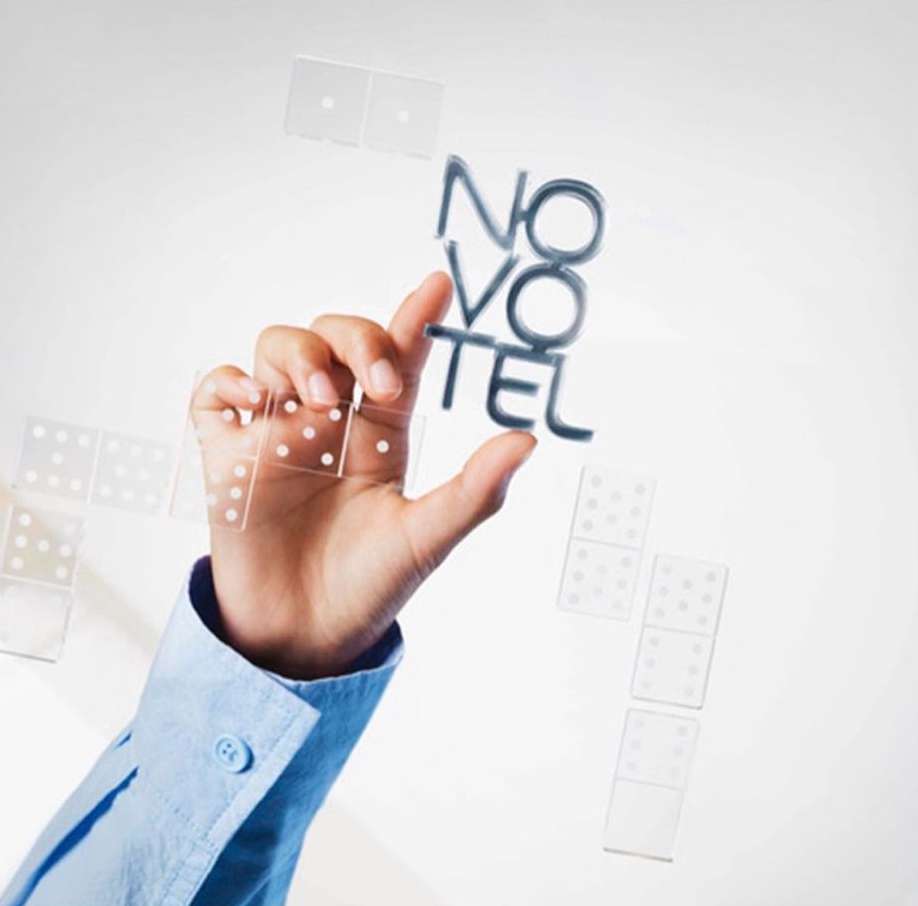 Human hand manipulating translucent dominoes and the word 'Novotel' against a white background. Studio shot with clear focus.