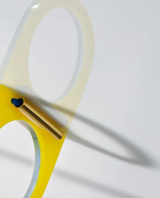 Abstract still life shot featuring a yellow and white frame with geometric shapes and a gold metal cylinder on a white background.