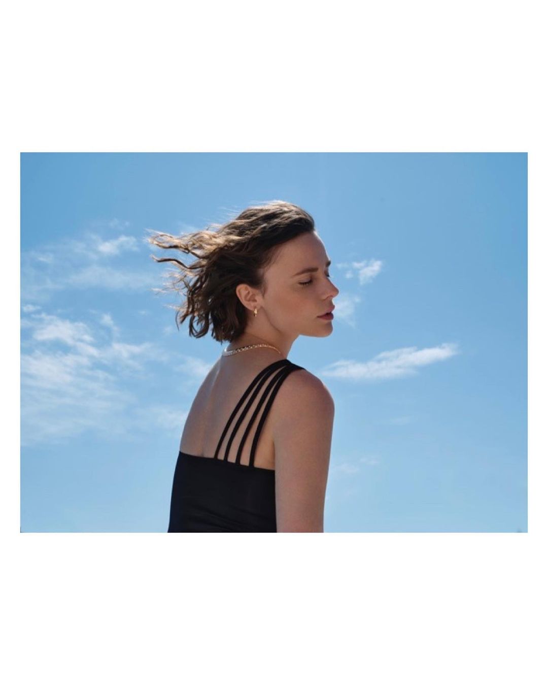 Profile view of a woman with dark hair in a black strap top against a clear blue sky by Laura Bonnefous