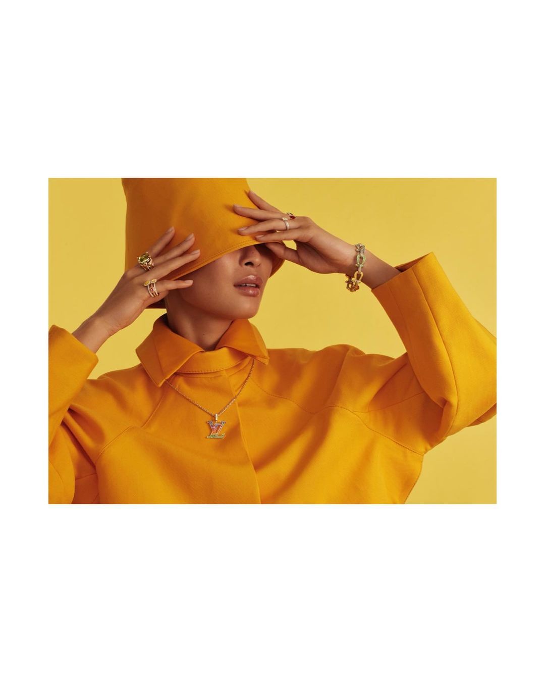 Woman wearing a yellow hat and coat with jewelry. Fashion shot on yellow background with a model, rings, necklace, and bracelet.