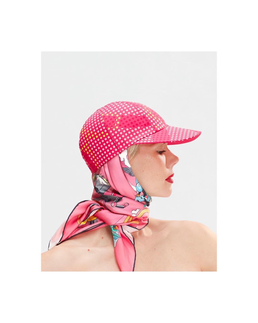 Profile portrait of a woman wearing a pink polka dot cap and a vibrant silk scarf around her neck against a plain background