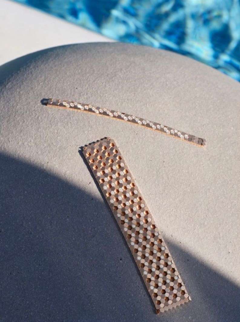 Close-up of two patterned textured surface materials in neutral tones. One is a strip with repeating hole design; the other is a thin rod.