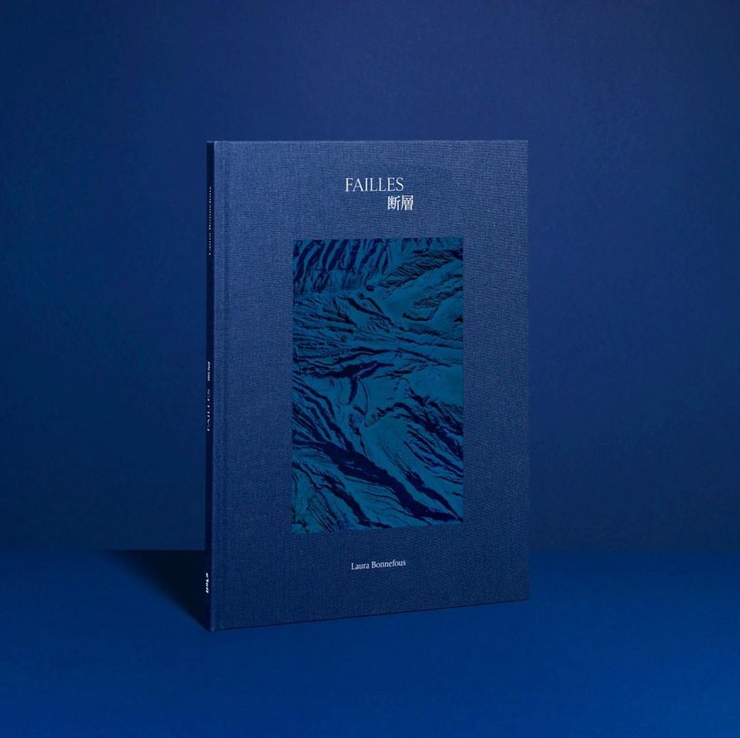 A book cover in shades of blue features an abstract design in a rectangular frame, with the title and author's name printed on the cover.