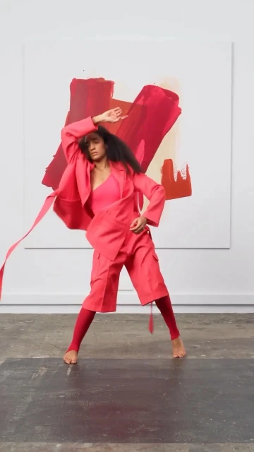 Woman in pink suit strikes dynamic pose in front of abstract painting in bright studio. Fashion editorial style with contemporary flair.