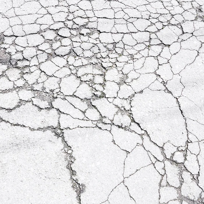 Close-up view of weathered white concrete with an intricate network of deep cracks and textured fissures across the surface.