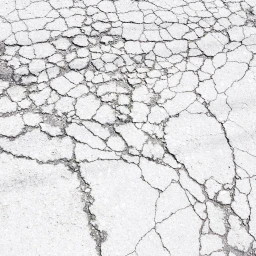 Close-up view of weathered white concrete with an intricate network of deep cracks and textured fissures across the surface.