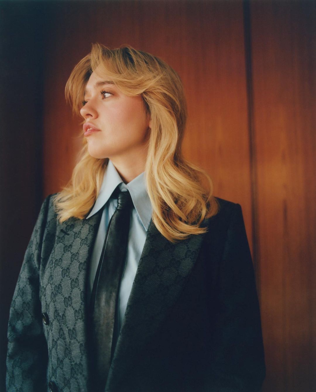 Portrait of Florence Pugh with blonde hair wearing a patterned blazer, light blue shirt, and dark tie by Laura Mccluskey