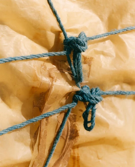 Close-up of blue twine knotted around a wrapped parcel with yellowing paper, casting shadows and suggesting an aged package.