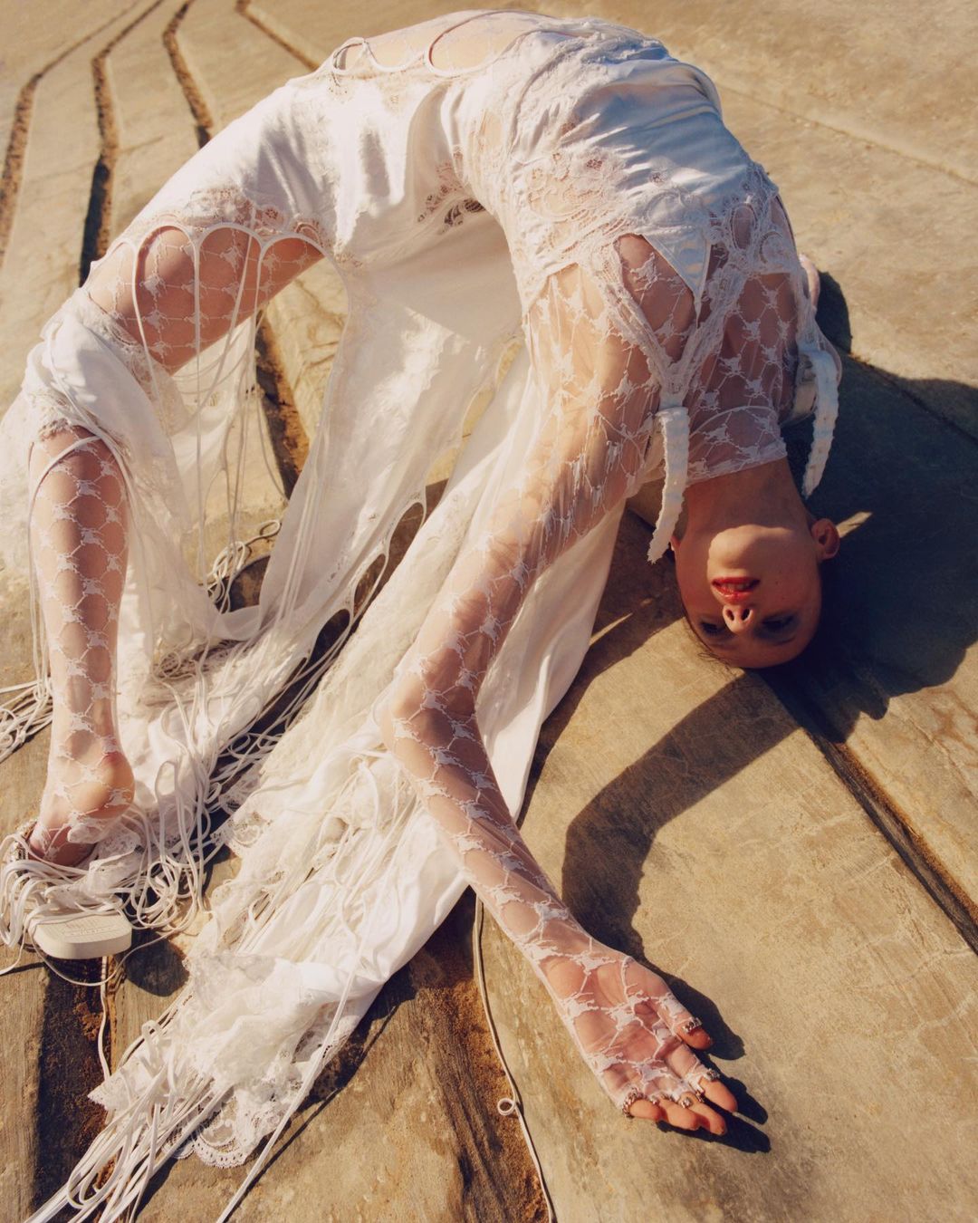 Model in white lace dress bending backwards on a concrete structure in London by photographer Laura Mccluskey
