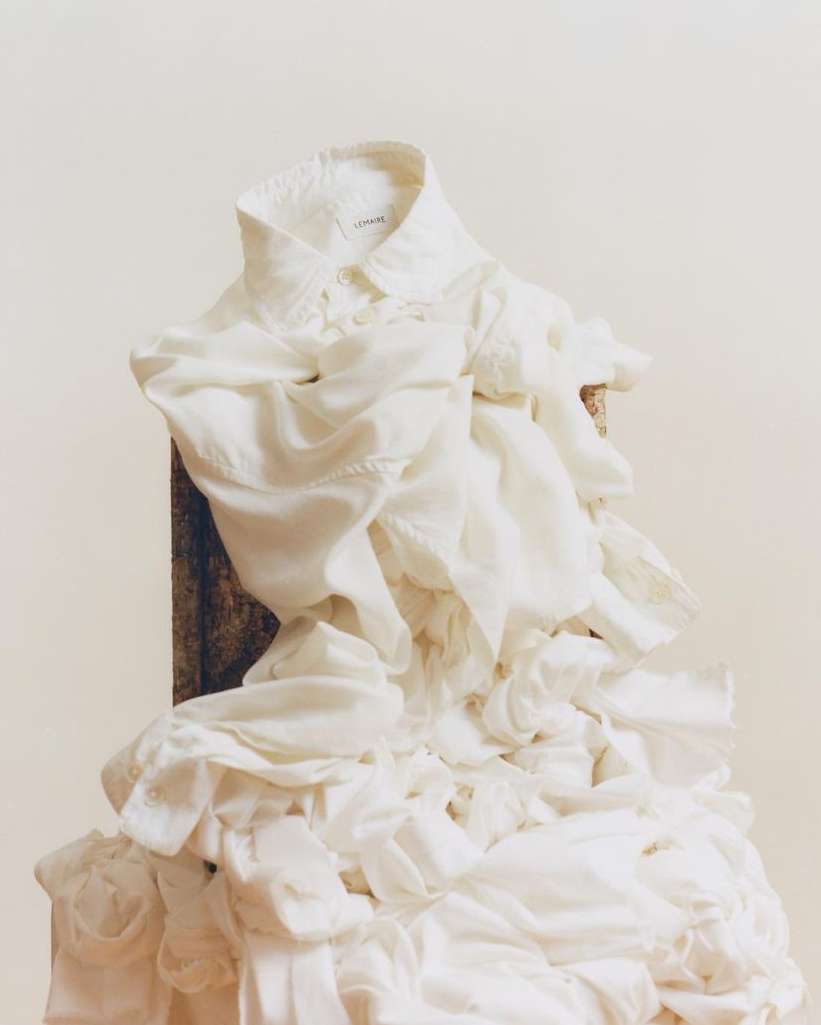 White collared shirt with cascading ruffles on a wooden surface against a light beige background. The focus is on the fabric's texture.