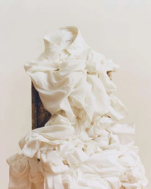 White collared shirt with cascading ruffles on a wooden surface against a light beige background. The focus is on the fabric's texture.