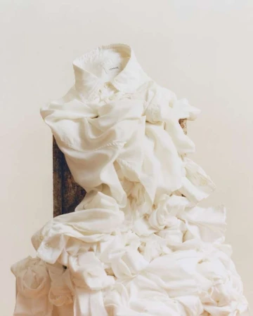 White collared shirt with cascading ruffles on a wooden surface against a light beige background. The focus is on the fabric's texture.
