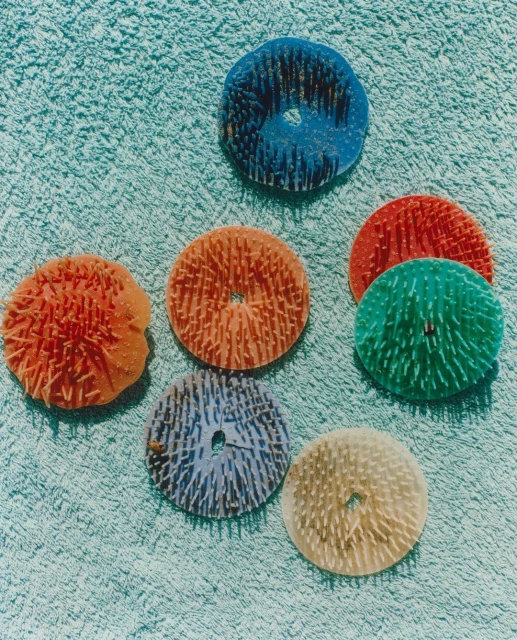 Overhead shot of colorful, round cleaning scrub pads with spikey textures arranged on a light blue terry cloth towel surface.