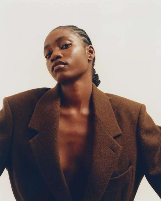 Elegant portrait of an African-American woman wearing a brown blazer against a plain white background in a studio fashion shot.