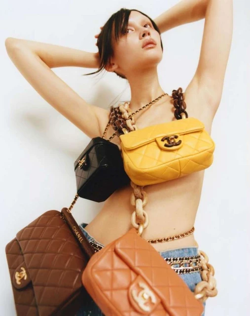Fashion shot of an East Asian female model wearing a Chanel branded crossbody chain with quilted handbags in a white studio setting.