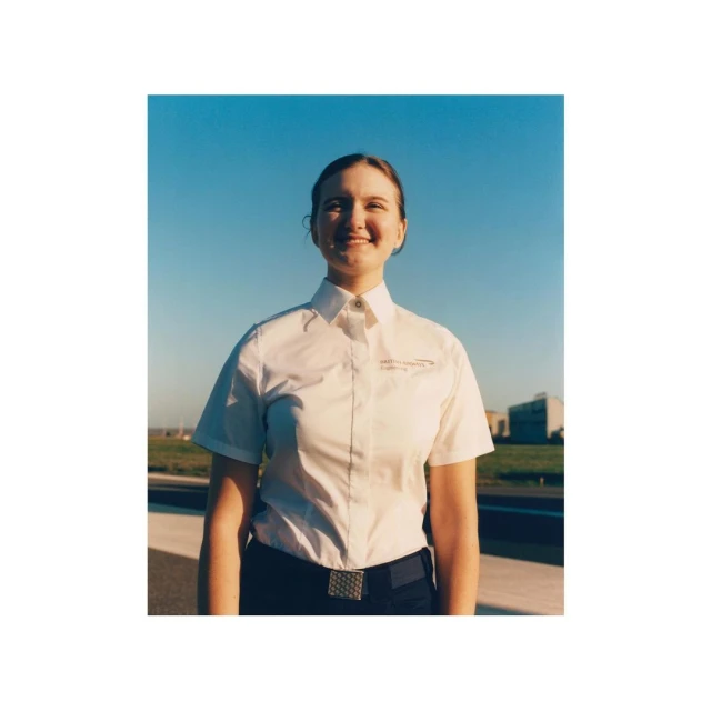Headshot of a smiling adult female in a collared shirt with short sleeves, photographed outdoors on a sunny day with blue skies.