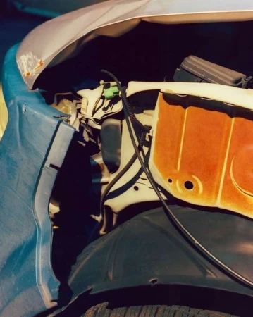 Damaged front end of a silver car with blue bumper and orange engine area, tire is also visible. The car appears to be wrecked.