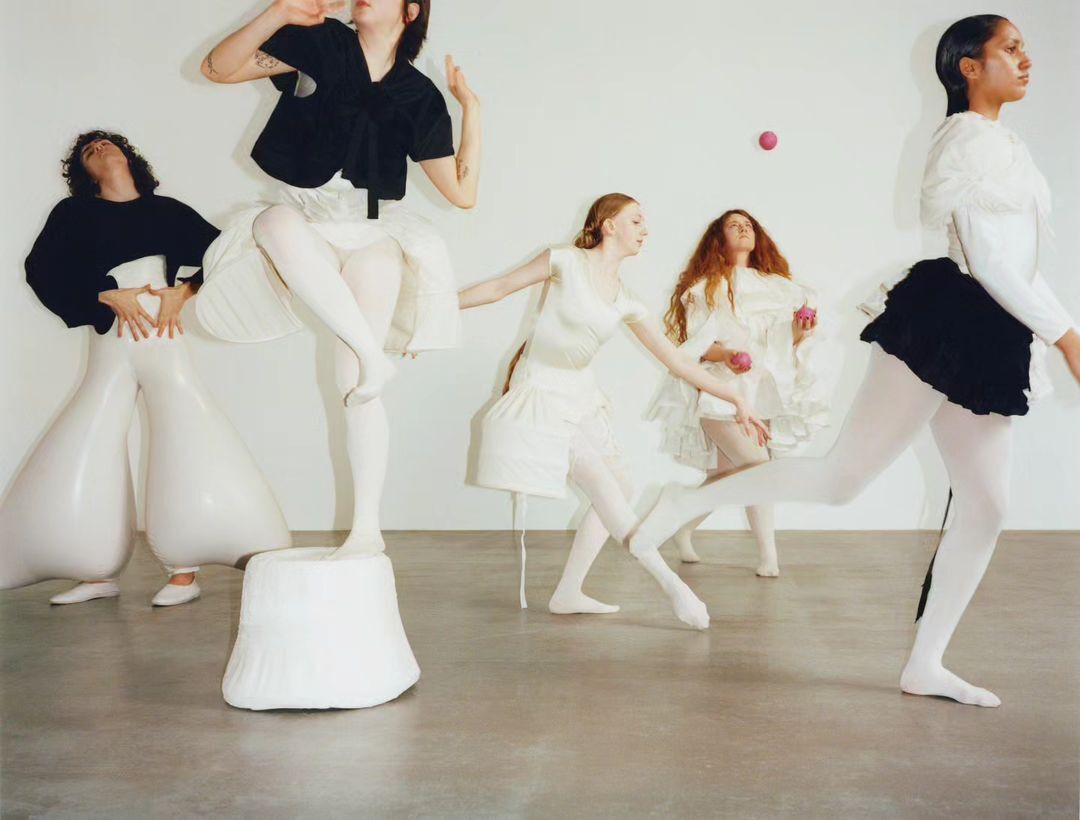Group of five female fashion models in white and black avant-garde dresses in a photo studio, posing with pink balls.