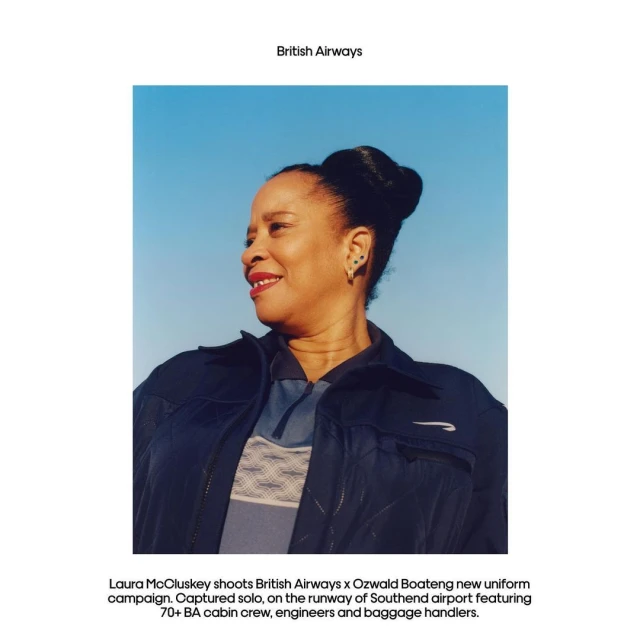 Smiling African-American woman in British Airways uniform against a blue sky, photographed in natural light with a shallow depth of field.