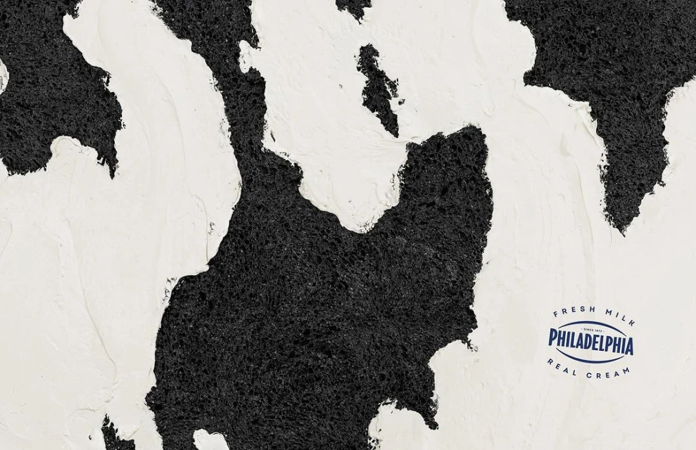 Creamy white topping swirls over a dark, textured surface, creating an abstract design with the Philadelphia Cream Cheese logo.