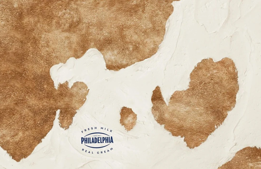 Close-up of a textured surface with white and brown sections, resembling a cowhide pattern, with the Philadelphia Cream Cheese logo.
