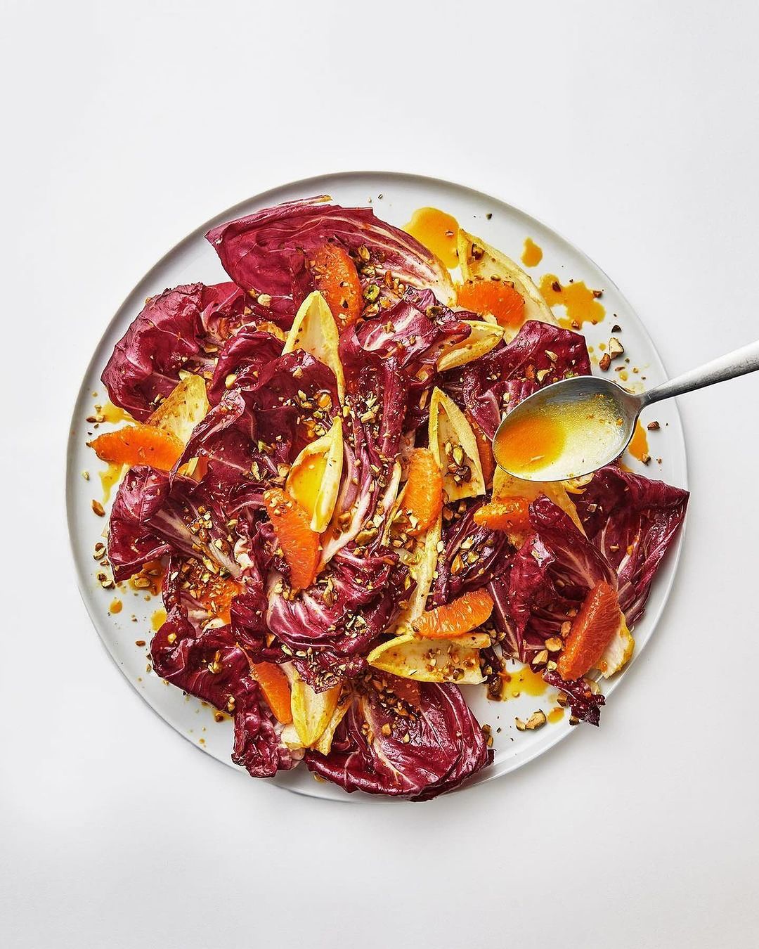 Radicchio salad with orange slices and dressing on a plate, top-down studio shot, vibrant colors, and appetizing presentation.