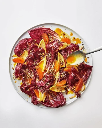 Radicchio salad with orange slices and dressing on a plate, top-down studio shot, vibrant colors, and appetizing presentation.