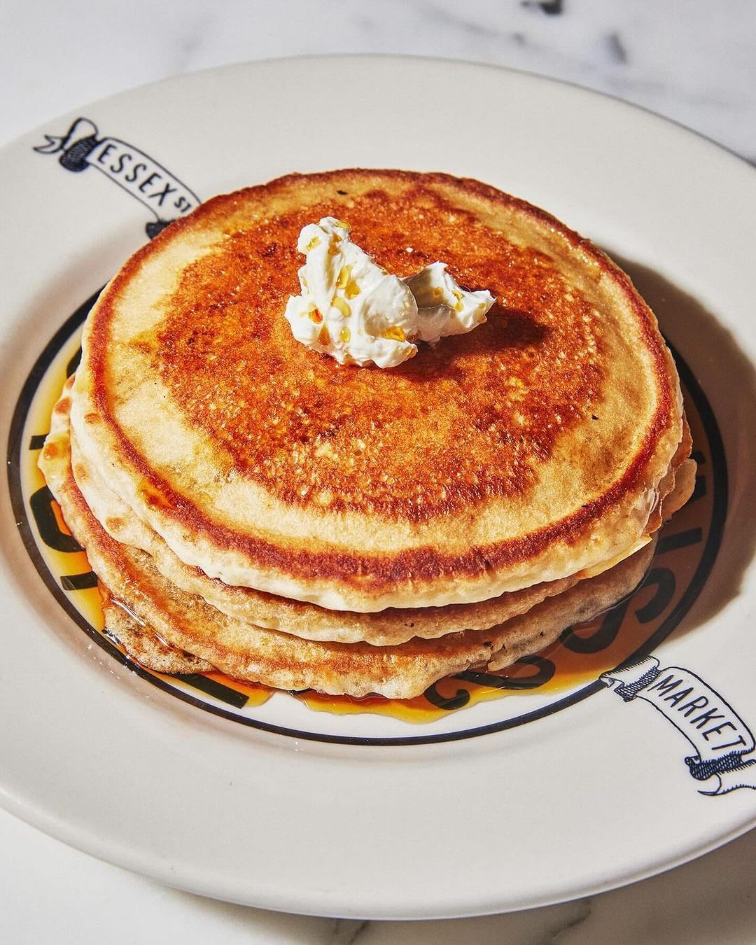 Overhead shot of stack of pancakes topped with butter and syrup on a white plate from Essex Street Market. Food and beverage.