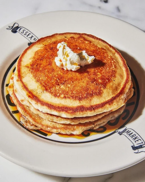 Overhead shot of stack of pancakes topped with butter and syrup on a white plate from Essex Street Market. Food and beverage.
