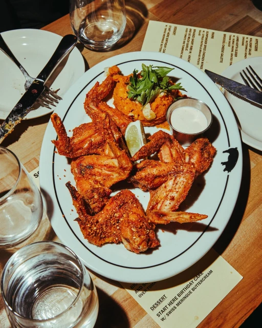 Overhead shot of fried chicken wings served on a plate with a side of sweet potato and cream sauce, complemented by drinks and cutlery.