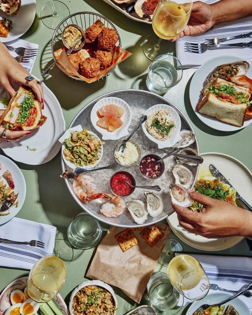 Overhead shot of a table with various seafood dishes, sandwiches, and beverages arranged on plates and a metal serving tray.