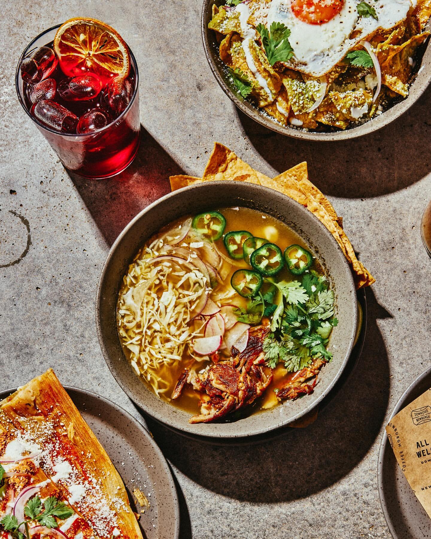 Overhead view of four plates and bowls showcasing diverse culinary dishes and drinks on a textured concrete surface.