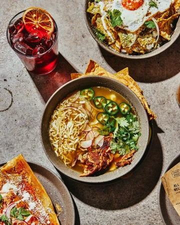 Overhead view of four plates and bowls showcasing diverse culinary dishes and drinks on a textured concrete surface.