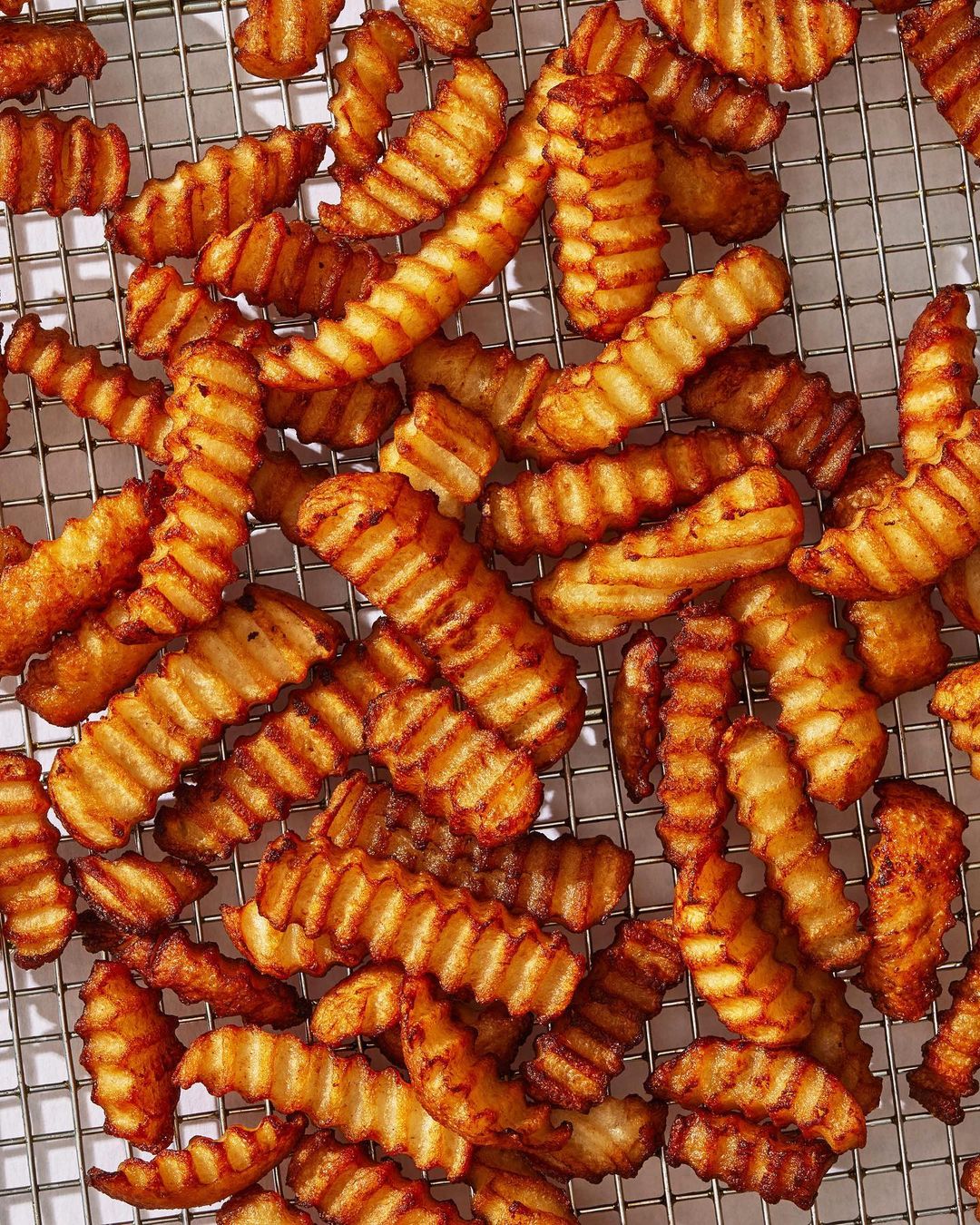 Overhead shot of crispy, golden-brown crinkle-cut French fries arranged on a wire rack, showcasing texture and preparation.