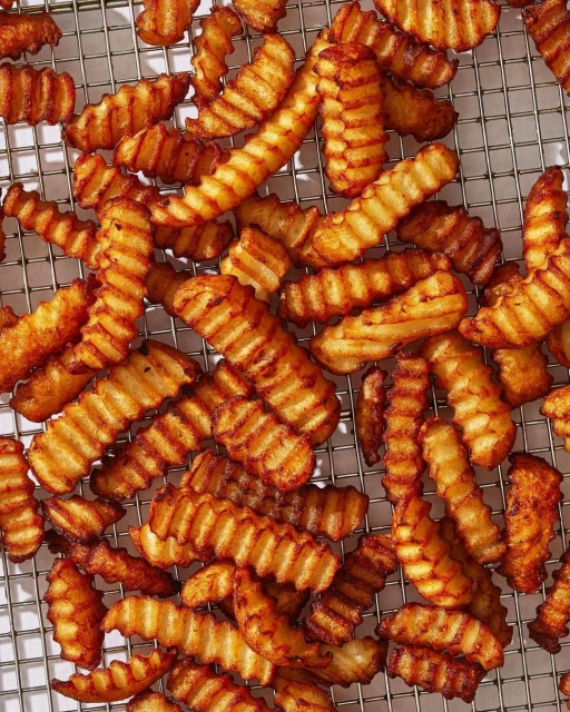 Overhead shot of crispy, golden-brown crinkle-cut French fries arranged on a wire rack, showcasing texture and preparation.