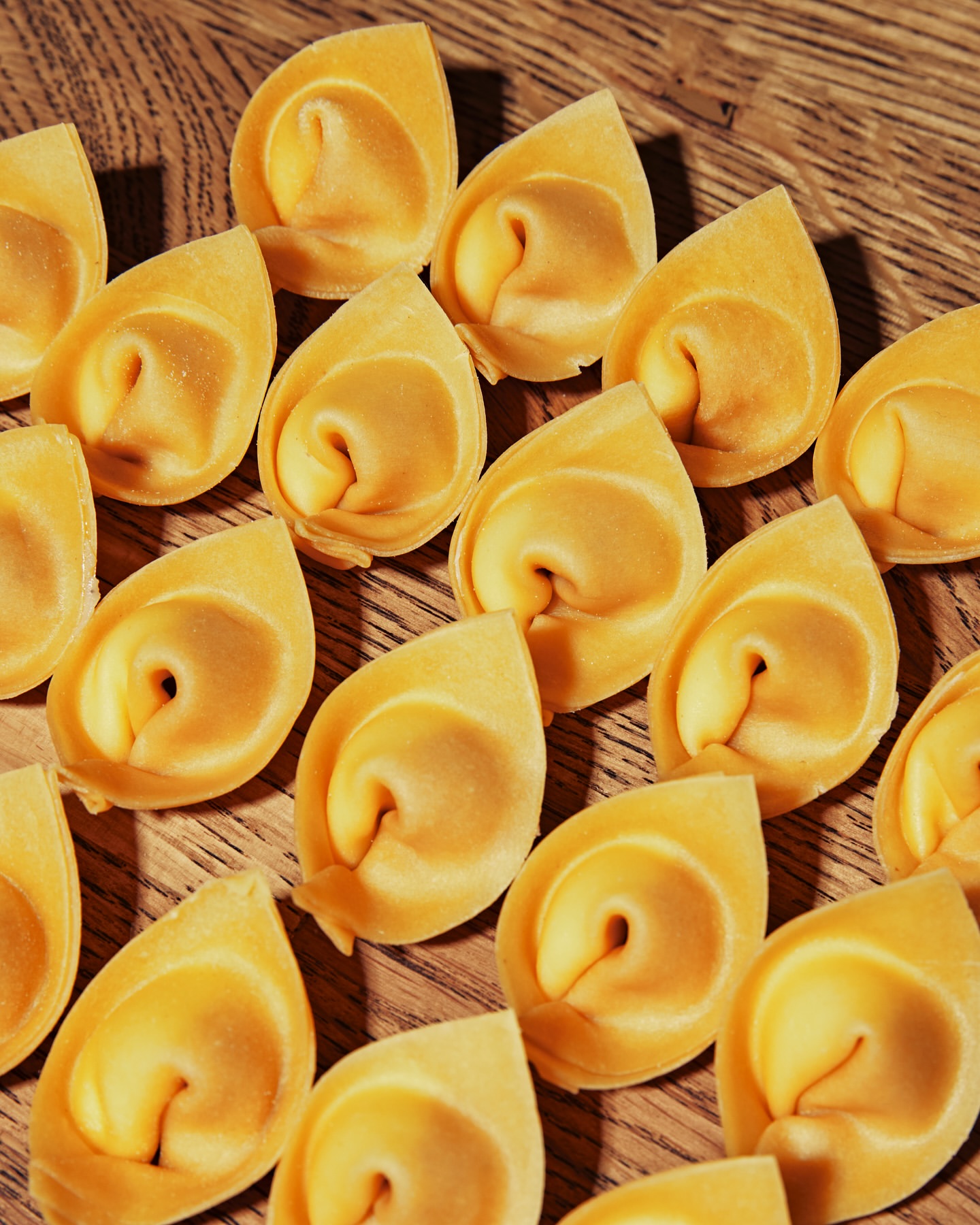 Close-up of numerous fresh tortelloni pasta pieces arranged on a wooden surface, creating a textured food background.