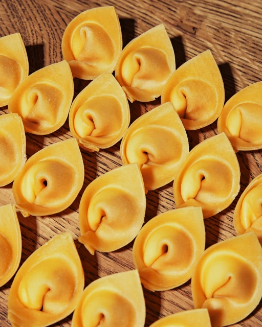 Close-up of numerous fresh tortelloni pasta pieces arranged on a wooden surface, creating a textured food background.