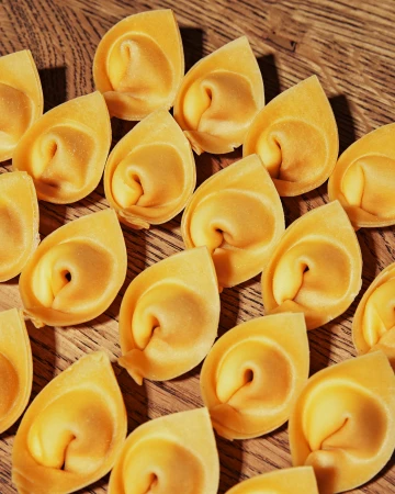 Close-up of numerous fresh tortelloni pasta pieces arranged on a wooden surface, creating a textured food background.