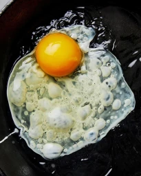 Close-up of a fried egg with a bright yellow yolk and bubbling white cooking in a dark skillet by photographer Laura Murray.