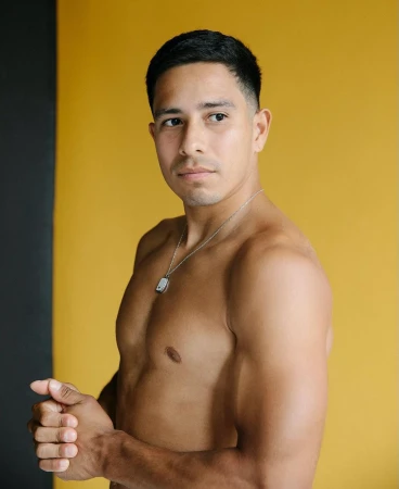 Portrait of a shirtless man wearing a silver pendant necklace against a yellow and black studio background