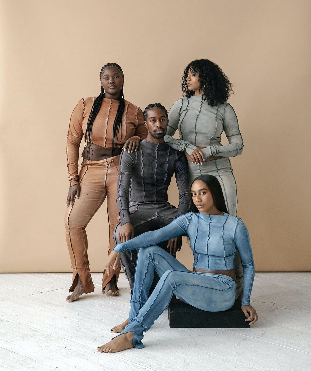 Group of four diverse fashion models in color-coordinated outfits in a studio setting, showcasing modern style and individual poses.