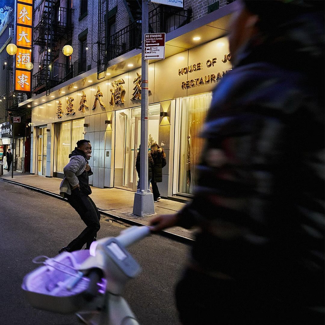 Busy Chinatown street scene with a pedestrian walking past a restaurant under warm lighting, with a bicycle in the foreground.