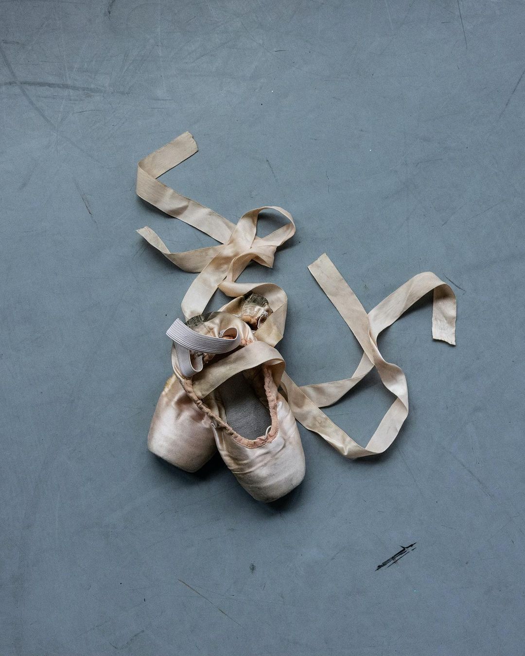 Ballet pointe shoes with long ribbon on grey surface. Dance footwear in neutral pink tones, soft texture, and muted colors.