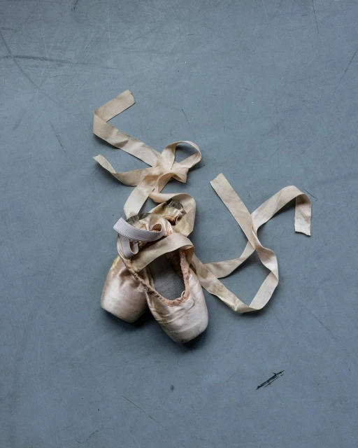 Ballet pointe shoes with long ribbon on grey surface. Dance footwear in neutral pink tones, soft texture, and muted colors.