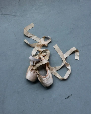 Ballet pointe shoes with long ribbon on grey surface. Dance footwear in neutral pink tones, soft texture, and muted colors.